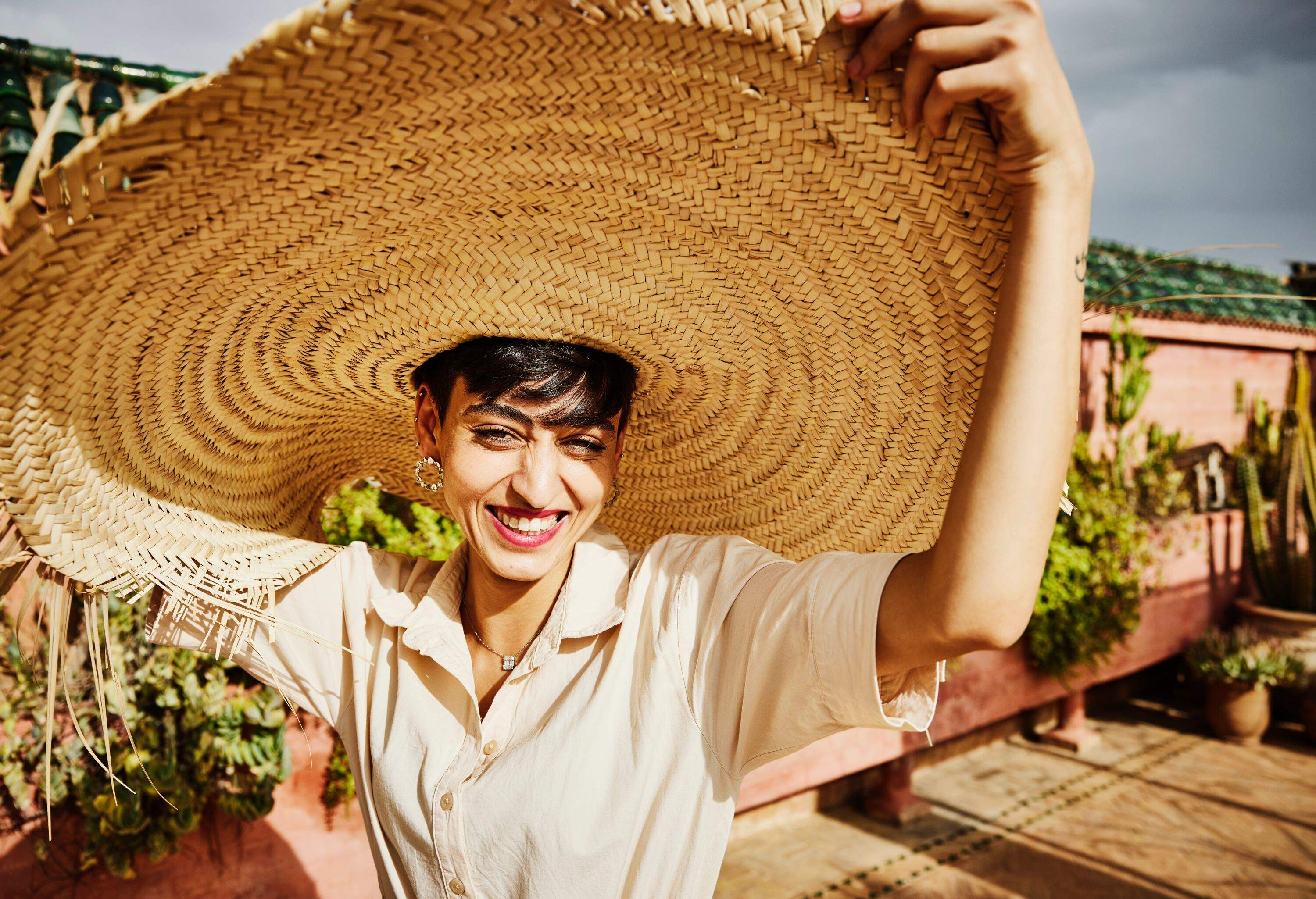 Medium shot portrait of smiling woman wearing large sunhat on rooftop of riad while on vacation in Marrakech