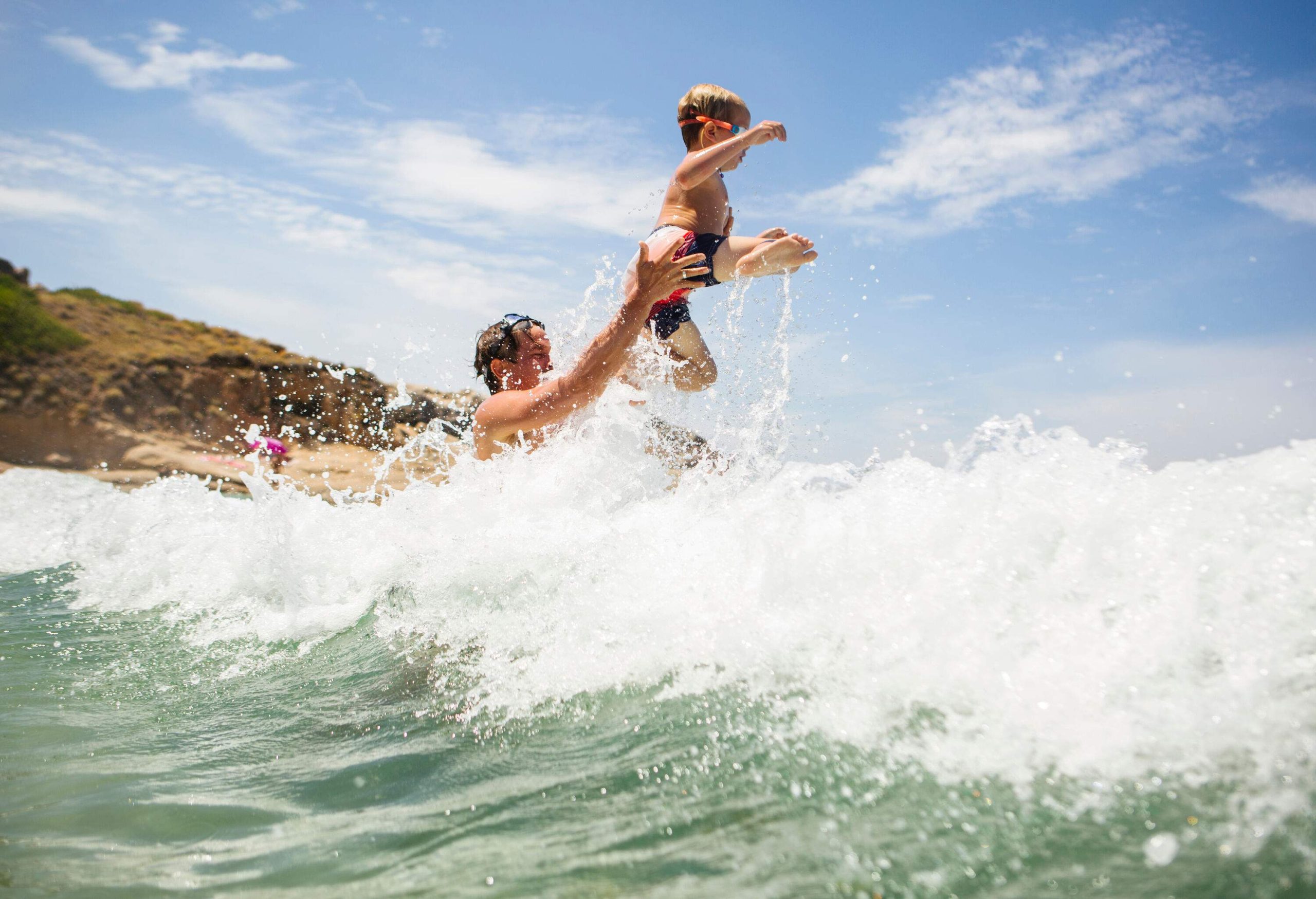 Man lifts a kid above the raging waves of the sea.