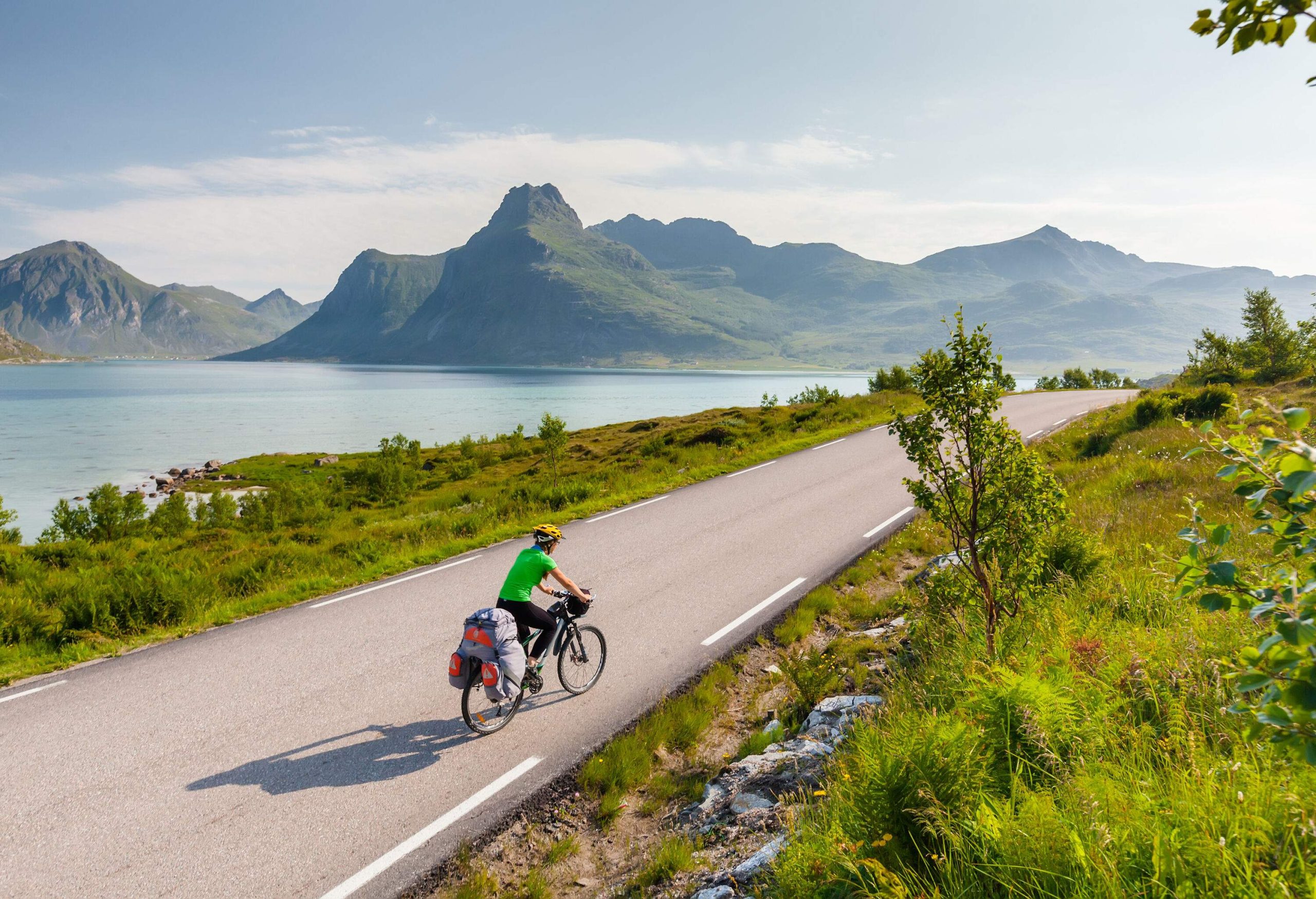 A person rides a loaded bike on a road with lake and mountain views.