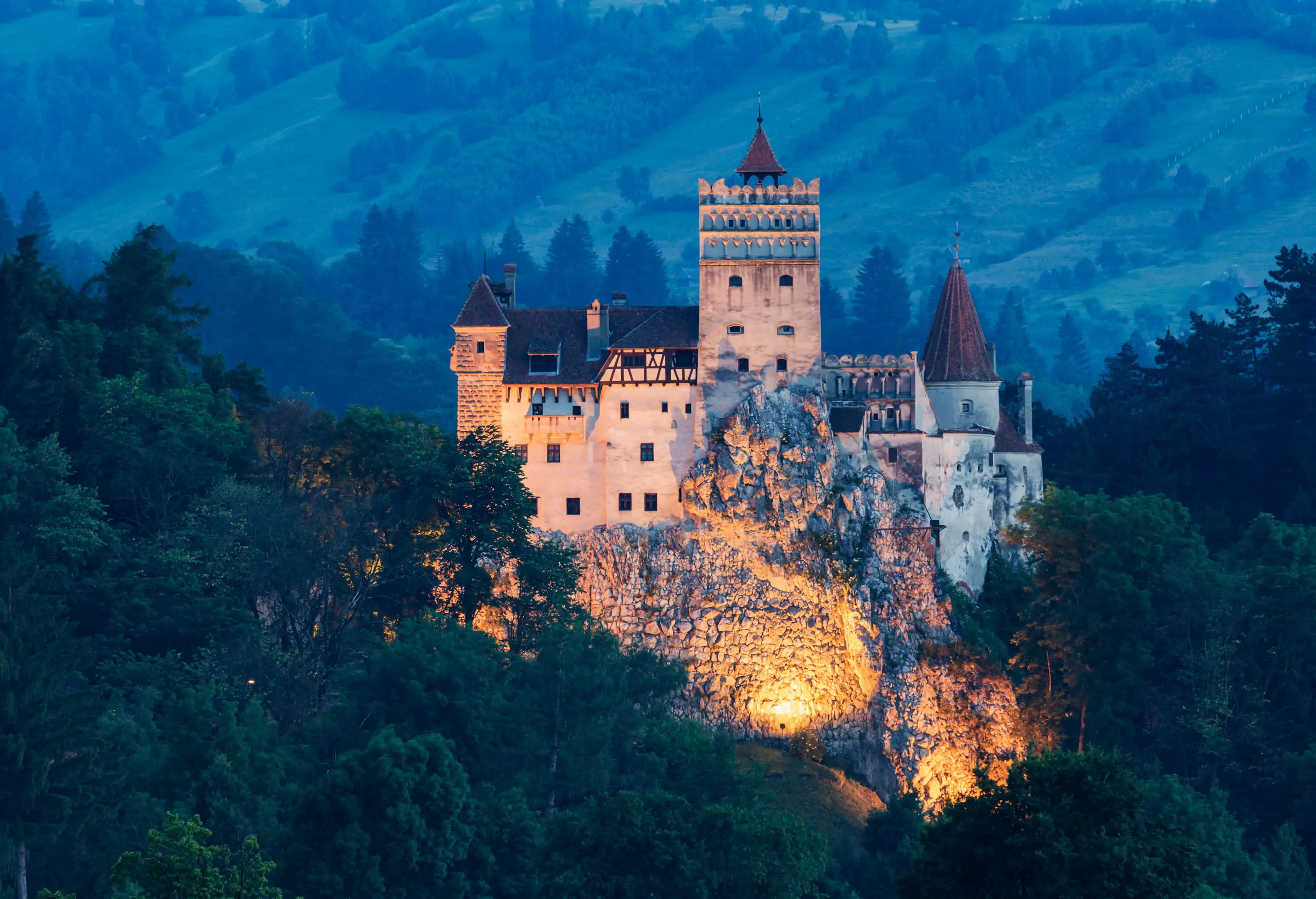 A historic stone castle with spired turrets surrounded by lush forests.